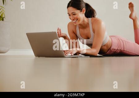 Istruttore di allenamento che comunica con la classe durante la videochiamata in palestra. Allenatore di fitness femminile sorridente in videochiamata sul suo laptop. Foto Stock