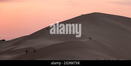 Vista panoramica delle persone che si arrampicano sulle enormi dune di sabbia di Badr, Medina, in Arabia Saudita al tramonto. KSA Turismo Foto Stock