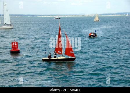 Piccolo yacht con scafo nero e vele rosso/arancio e due uomini a bordo durante la regata della settimana di Cowes, Inghilterra Foto Stock