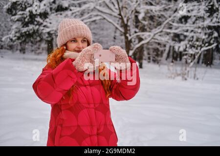Una donna felice tiene un iphone di mela nelle sue mani, un parco invernale con alberi nella neve Foto Stock