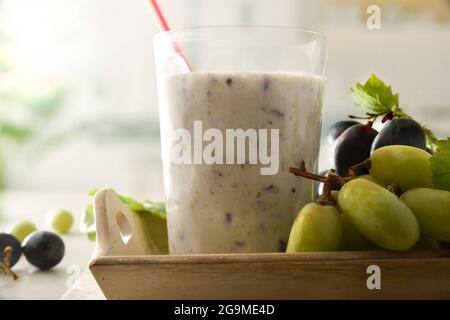 Yogurt biologico liquido all'uva su piatto bianco con grappoli di uve bianche e rosse in prova su tavolo di legno con fondo cucina. Vista frontale. Foto Stock