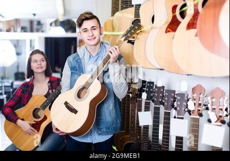 Inglese per teenager ai clienti di decidere su appositi chitarra acustica nel negozio di chitarra Foto Stock