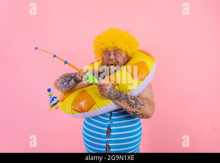 Grasso uomo stupito con parrucca in testa gioca con la canna da pesca Foto Stock