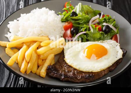 Bistecca di manzo con uova, patatine fritte, riso e insalata nel piatto sul tavolo. Orizzontale Foto Stock