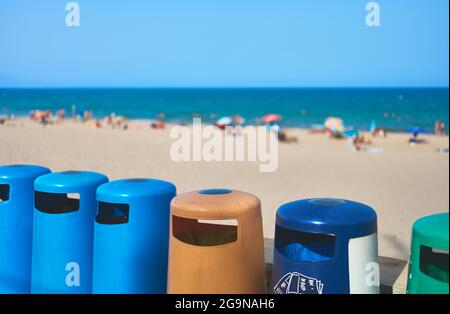 particolare di contenitori di rifiuti di fronte ad una spiaggia con turisti con mare e cielo blu Foto Stock