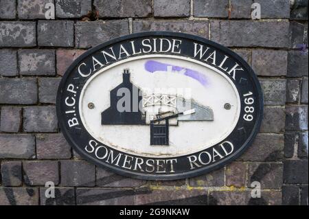 Placca ovale in ghisa sulla parete in mattoni del ponte sopra il canale di Worcester e Birmingham a Somerset Road che segna una passeggiata a lato del canale, Birmingham, Inghilterra. Foto Stock