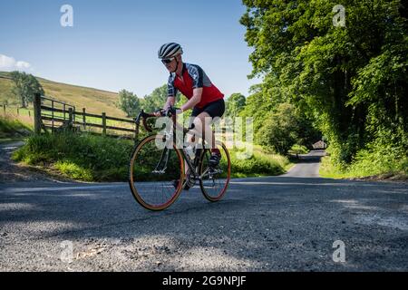 Un ciclista maschile maturo che sale sulla collina da Whitewell, Bowland, Lancashire, Regno Unito. Foto Stock