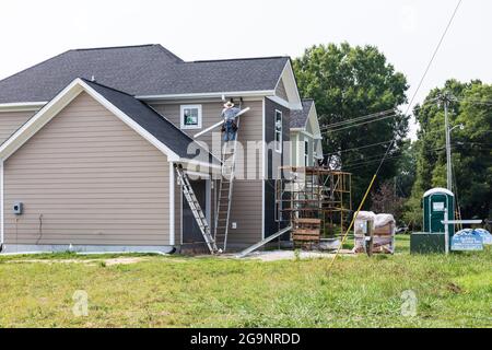 HICKORY, NC, USA-22 LUGLIO 2021: Una nuova casa del patio in costruzione che mostra un operaio che si monta grondaie, e impalcature. Foto Stock