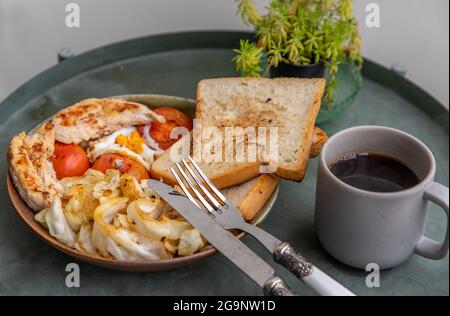 Colazione con pollo al forno, uova fritte, pomodoro, pane tostato e cavolo fritto su piatto di ceramica servito con caffè nero. Focalizzazione selettiva. Foto Stock