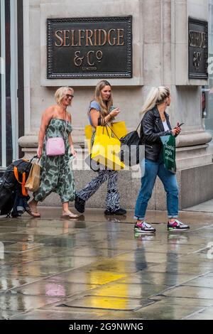 Londra, Regno Unito. 27 luglio 2021. Ripararsi da una tempesta può anche essere appropriato come la pioggia cade sugli acquirenti - 'fare fieno mentre il sole splende' è uno slogan sulle finestre di Selfridges che ora è stato messo in vendita al più alto offerente. Credit: Guy Bell/Alamy Live News Foto Stock