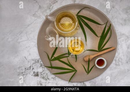 Rinfrescatevi e gustatevi con UNA tazza di tisana di Cannabis e gambo con foglie di marijuana verde con miele sul tavolo di marmo per scopi medici per dormire Foto Stock