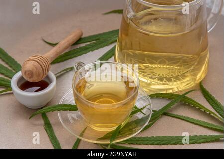 Rinfrescatevi e gustatevi con UNA tazza di tisana di Cannabis e gambo con foglie di marijuana verde con miele sul tavolo di marmo per scopi medici per dormire Foto Stock