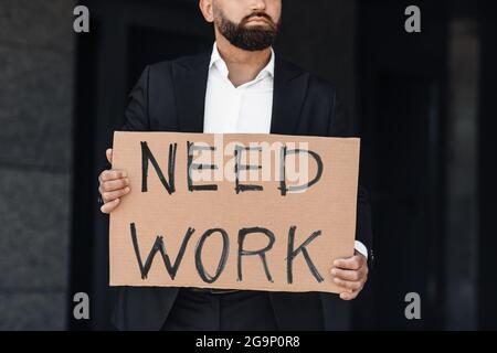 Ha bisogno di lavoro. Operaio maschile irriconoscibile in cartoncino, in piedi all'aperto vicino al business center, raccolto Foto Stock