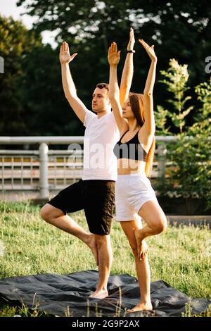 Giovane coppia uomo e donna che fa sport, yoga sul prato della città, estate sera, stretching Foto Stock