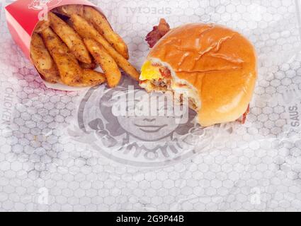 Wendy's baconator colazione Sandwich su wrapper con morso preso e patate condite con pancetta, uova, salsiccia e formaggio Foto Stock