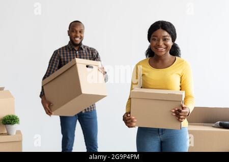 Gioioso sposi neri che trasportano le scatole con gli effetti personali durante il trasferimento al nuovo appartamento Foto Stock