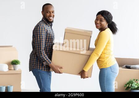 Concetto di riposizionamento domestico. Gioiosi sposi neri che portano scatole di cartone nella loro casa Foto Stock