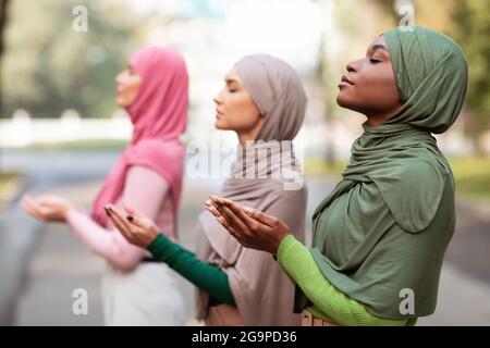 Gruppo di tre diverse donne islamiche che pregano all'aperto indossando Hijab Foto Stock