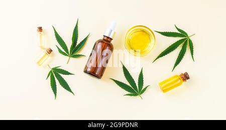 Gruppo di bottiglie di vetro, contagocce e ciotola con olio cbd di cannabis, tintura thc e foglie di canapa. Vista dall'alto, disposizione piatta Foto Stock