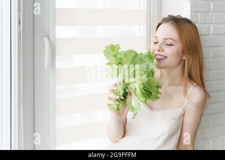 giovane donna con un mazzo di lattuga in una stanza bianca. stile di vita sano, vegetarianismo Foto Stock