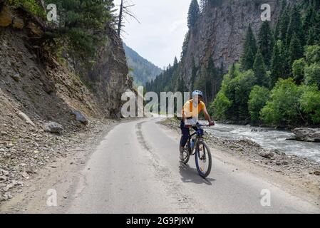 Un ciclista che corre lungo una strada tra le montagne a Tulail. Gurez si trova lungo la LOC (linea di controllo) nella parte settentrionale del Kashmir. La Valle di Gurez fu la chiave della Via della Seta dall'Europa al Kashgar in Cina e patria della tribù dei Dard di lingua shina, ma non fu aperta al mondo fino al 2007. Prima del 2007, Gurez era aperto solo durante il periodo coloniale, quando i viaggiatori sono venuti per esplorare la valle. La linea di controllo ora attraversa la valle idilliaca, separando i dardi dai loro fratelli Indo-ariani a Gilgit, Chilas e Astore che si trovano in Pakistan. Foto Stock