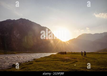 Gli uomini hanno visto camminare durante il tramonto a Dawar. Gurez si trova lungo la LOC (linea di controllo) nella parte settentrionale del Kashmir. La Valle di Gurez fu la chiave della Via della Seta dall'Europa al Kashgar in Cina e patria della tribù dei Dard di lingua shina, ma non fu aperta al mondo fino al 2007. Prima del 2007, Gurez era aperto solo durante il periodo coloniale, quando i viaggiatori sono venuti per esplorare la valle. La linea di controllo ora attraversa la valle idilliaca, separando i dardi dai loro fratelli Indo-ariani a Gilgit, Chilas e Astore che si trovano in Pakistan. Foto Stock