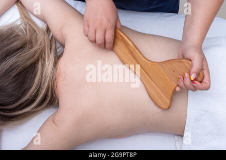 Le mani femminili massaggiano la schiena del paziente con un massaggiatore in legno, primo piano. Donna che ha un massaggio termale al salone di bellezza. Trattamento schiena con massaggio, Foto Stock