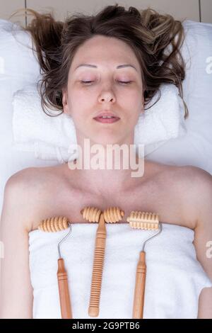 Madero terapia, massaggio rilassante anticellulite - massaggiatori in legno rulli a spillo, rullo liscio adagiato su un asciugamano bianco su una donna, vista dall'alto, clos Foto Stock