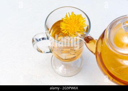 Versare il tè al dente di leone alle erbe in una tazza trasparente da una teiera su sfondo bianco, primo piano. Sano tè alle erbe nelle calde giornate estive. Spegnimento Foto Stock