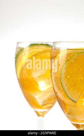 Due bicchieri a gambo con tè ghiacciato e fette di limone e lime su bianco Foto Stock