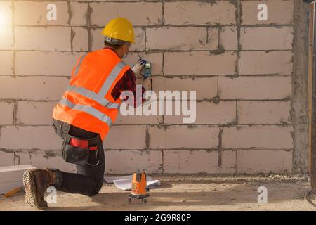 Tecnico con livello di misurazione laser durante il lavoro,addetto alla costruzione che misura il raggio di supporto durante il tramonto Foto Stock