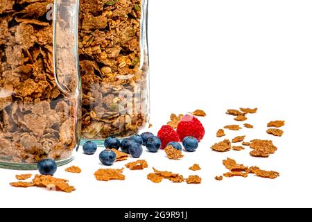 Isolare muesli. I fiocchi di muesli secchi con lamponi e mirtilli si trovano su uno sfondo bianco isolato. Colazione cereali in un vaso di vetro su un bianco Foto Stock