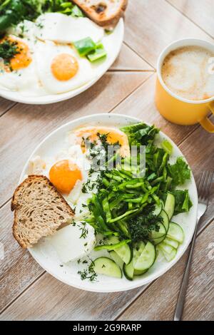 Uova fritte, pane e verdure verdi per la colazione, servite con una tazza di caffè su un tavolo di legno Foto Stock