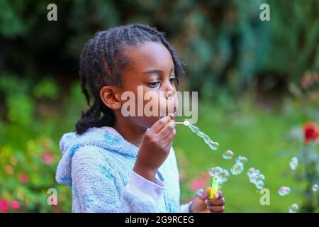 Una giovane ragazza nera che soffia delle bolle Foto Stock