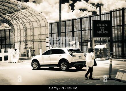 In bianco e nero drammatico, UNA donna in traversata con segno digitale in spagnolo e veicolo al confine tra Stati Uniti-Messico, Douglas, AZ, Stati Uniti Foto Stock