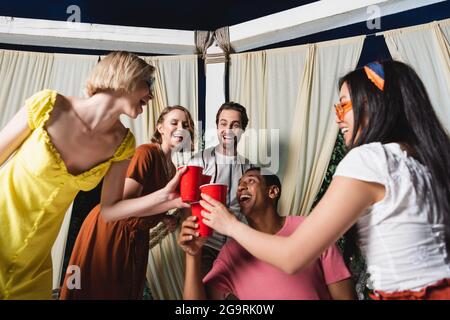 Amici interrazziali tostare con tazze di plastica nel patio Foto Stock