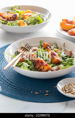 Primo piano di un'insalata di pesche e arugula alla griglia servita con prosciutto e condita con semi di girasole. Foto Stock