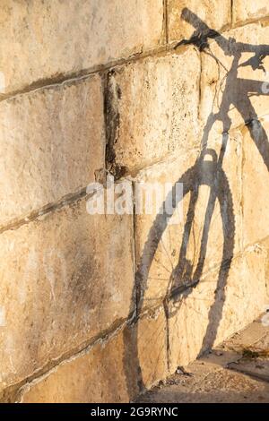 Ombra su un muro di pietra di una bicicletta parcheggiata su un molo in una giornata di sole Foto Stock