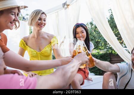 Felici persone multietniche che si aggraffano con bottiglie di birra nel patio Foto Stock