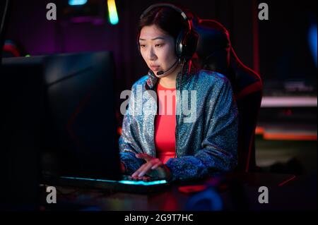 Un giovane giocatore cinese di eSport in un torneo internazionale di eSport. Un cyber team multirazziale sta giocando un gioco di sparatutto online. Luce al neon Foto Stock