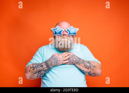 L'uomo grasso stupito con barba, tatuaggi e occhiali da sole è sorpreso per qualcosa Foto Stock