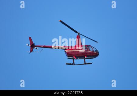 Un elicottero a turbina Robinson R66 è visto volare contro un cielo blu chiaro e senza nuvole. Foto Stock