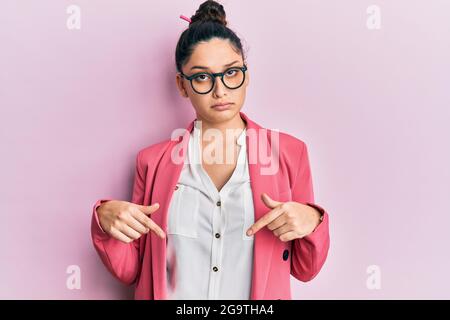 Bella donna medio orientale che indossa giacca e occhiali da lavoro che punta verso il basso guardando triste e sconvolto, indicando la direzione con le dita, infelice e. Foto Stock