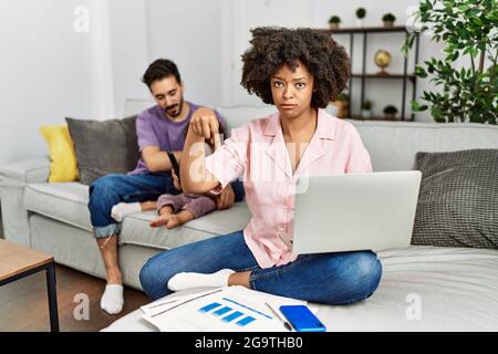 Madre di famiglia interracial che lavora usando il computer portatile a casa puntando giù guardando triste e sconvolto, indicando la direzione con le dita, infelice e. Foto Stock