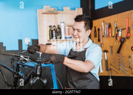 un meccanico di bicicletta in un grembiule che indossa guanti utilizzando una chiave a percussione Foto Stock