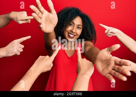 Bella donna afroamericana con i capelli afro con le dita intorno a se stessa guardando la macchina fotografica sorridente con le braccia aperte per abbraccio. Allegro Foto Stock