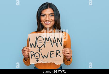 Giovane latino transessuale transgender donna che tiene il banner di potere donna che guarda positivo e felice in piedi e sorridente con un sorriso fiducioso che mostra te Foto Stock