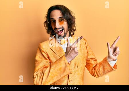 Giovane uomo ispanico che indossa l'hipster elegante look sorridente e guardando la fotocamera che punta con due mani e dita a lato. Foto Stock