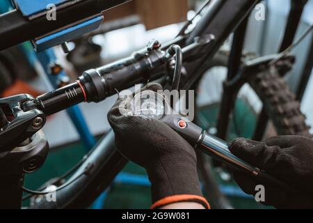 primo piano della mano di un meccanico di bicicletta nei guanti utilizzando una pompa per manometri per regolare la sospensione Foto Stock