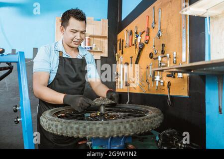 un meccanico di bicicletta in un grembiule che indossa guanti installa una ruota libera Foto Stock